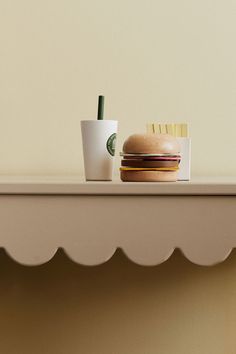 a hamburger, fries and drink sitting on a shelf in front of a white wall