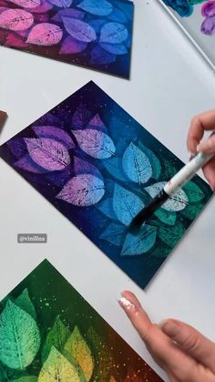 someone is painting leaves on paper with a paintbrush and watercolors in front of them