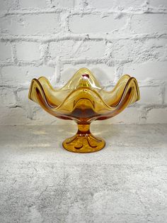 a yellow glass bowl sitting on top of a white table next to a brick wall