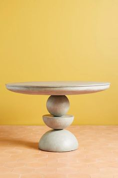 a white table topped with three stacked rocks on top of a tiled floor next to a yellow wall