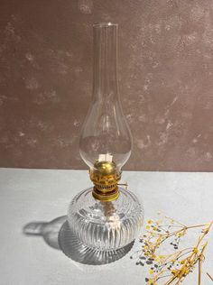 a clear glass vase with a gold top on a table next to dried yellow flowers