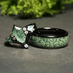 two wedding rings with green and white stones on them, sitting next to each other