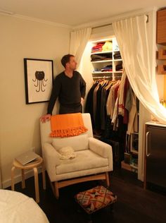 a man standing next to a white chair in a room with clothes on hangers