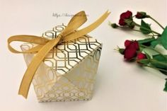 an origami box with a ribbon tied around it next to some red roses