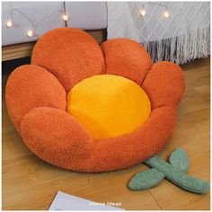 an orange flower shaped chair sitting on the floor next to a green dragon toy and white string lights