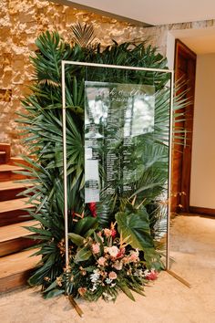 an arrangement of flowers and greenery on display in front of a glass frame at the bottom of stairs