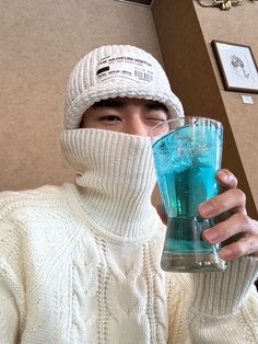 a man wearing a white hat and sweater holding a blue drink in front of his face