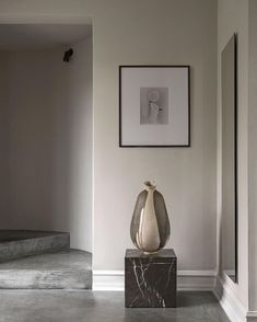 a white vase sitting on top of a marble block in front of a painting and stairs