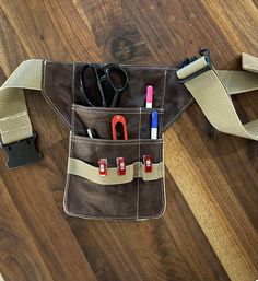 a brown bag with some scissors and other items in it on a wooden floor next to a pair of scissors