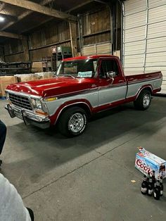 a red and silver truck parked in a garage next to two soda cans on the floor