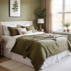 a bed with green sheets and pillows in a bedroom next to a window filled with potted plants