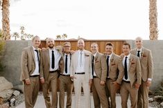 a group of men standing next to each other in front of a fence and palm trees