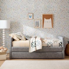 a day bed with pillows and blankets on it in front of a wallpapered room