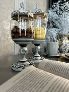 an open book sitting on top of a table next to two glass jars filled with food