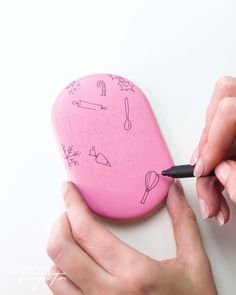 two hands are holding a pink object with writing on it and the other hand is using a black marker