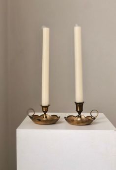 two candles sitting on top of a white box next to each other in front of a wall