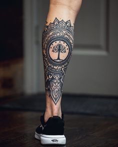 a person's leg with a tree and compass tattoo on the lower half of their leg