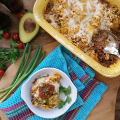 a casserole dish with meat, cheese and vegetables on a wooden cutting board