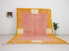 a pink and yellow rug sitting on top of a floor next to a potted plant