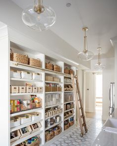 an organized pantry with lots of shelves and baskets on the bottom shelf, under a chandelier