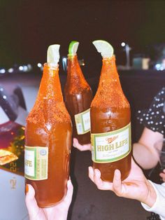 three bottles of beer are being held by two people at a table with food on it