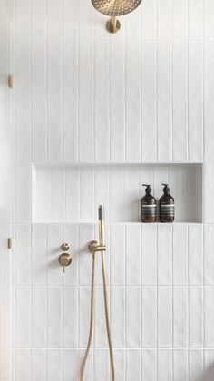 a white tiled shower with brass fixtures and soap dispensers on the wall