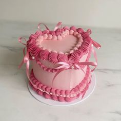 two pink heart shaped cakes on top of a white cake plate with ribbon around the edges