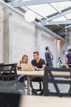 two people sitting at a table working on their laptops in an open room with exposed ceilings