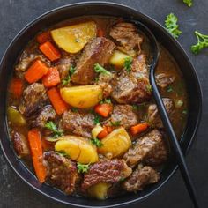 beef stew with carrots, potatoes and parsley in a black bowl on a dark surface