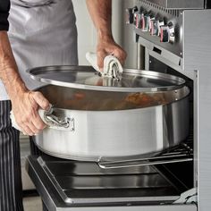 a man in an apron is using a large pot to cook food on the stove