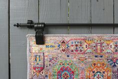 a multicolored rug hanging on a wall with a black metal hook in front of it