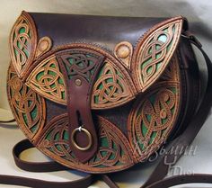 a brown and green leather purse with an intricate design on the front, sitting on a white surface