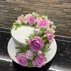 a white cake with pink and purple flowers on the top is sitting on a counter