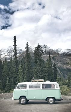 an old vw bus parked on the side of a road with mountains in the background