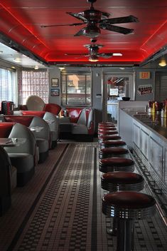 the interior of a diner with red and white lighting on the ceiling, chairs lined up against the bar