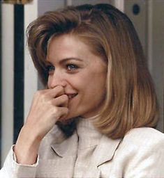 a woman in a white suit is smiling and holding her hand to her mouth while looking at the camera