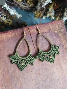 the earrings are made from green thread and beaded with gold beads, on top of a piece of wood