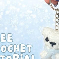 a white teddy bear keychain being held by a hand with snowflakes in the background