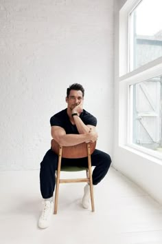 a man sitting on top of a wooden chair in front of a white brick wall