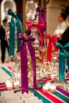 some candles are sitting on a table with glass jars and ribbons tied around the bottles