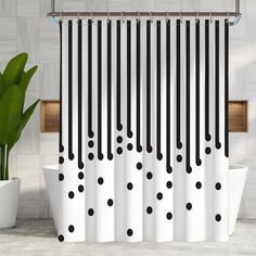 a shower curtain with black and white polka dots on it next to a potted plant