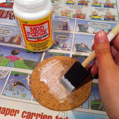 a hand holding a paint brush over a cookie on top of a newspaper with cartoon pictures