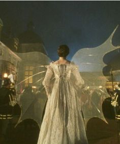 a woman in a white dress is standing outside at night with her arms outstretched and wings open