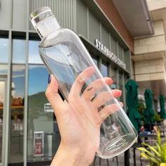 a hand holding a large clear water bottle in front of a building with green plants