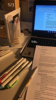 an open laptop computer sitting on top of a desk next to some pens and paper