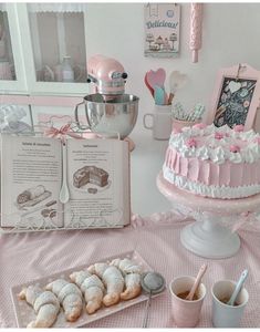 a pink cake sitting on top of a table covered in frosting next to an open book