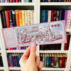 a person holding up a ticket in front of a book shelf with books on it