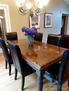 a dining room table with chairs and a vase filled with purple flowers on the top