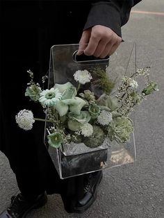 a person is holding a clear box with flowers in it while standing on the street