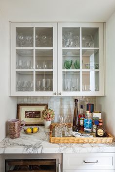 a kitchen with white cabinets and marble counter tops, filled with dishes and wine glasses